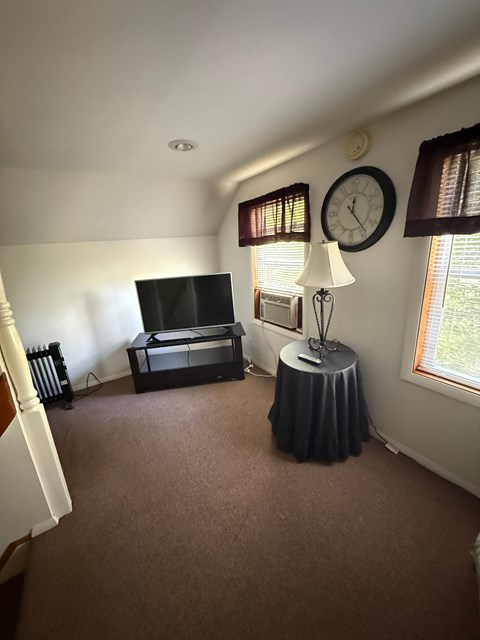 A living room with a television, a table with a lamp, and a clock on the wall.