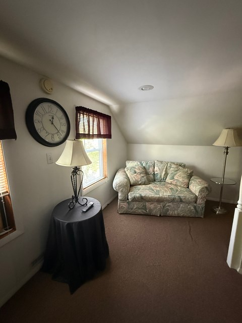A living room with a sofa, a table with a lamp and a clock on the wall.