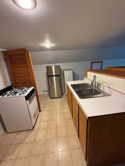 A kitchen with a stove, sink, and trash can.