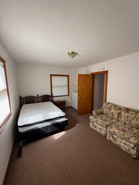 A bedroom with a bed, couch, and mirror.