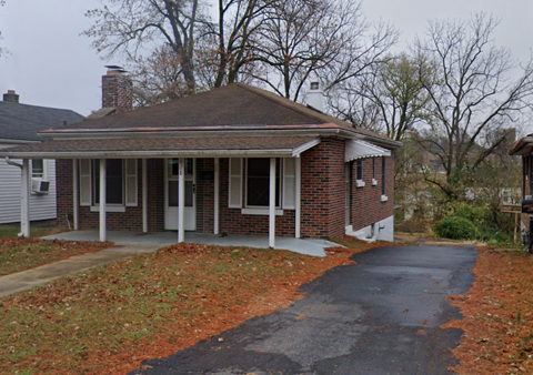 A house with a driveway and a tree in the background.
