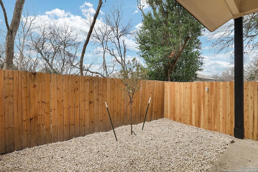 A backyard with a wooden fence and a small tree.