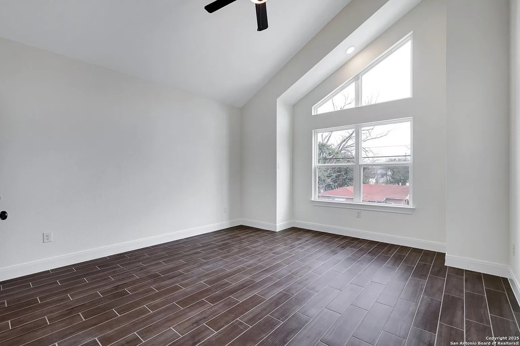 A room with a ceiling fan and a window overlooking a residential area.