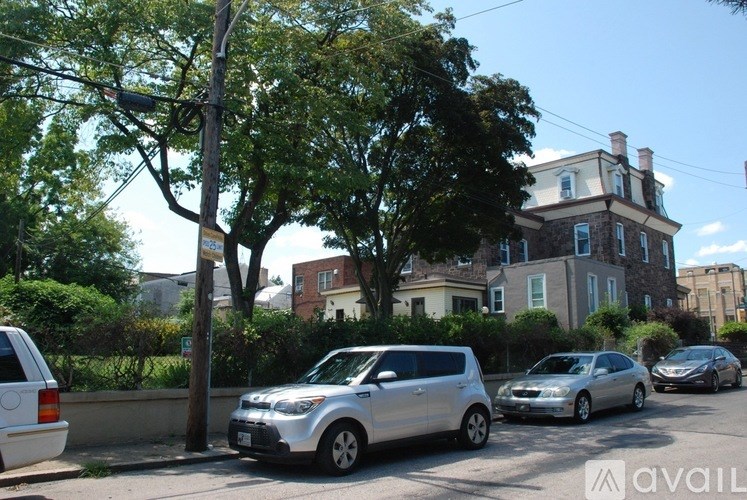 A street view with cars parked on the side and a large house in the background.