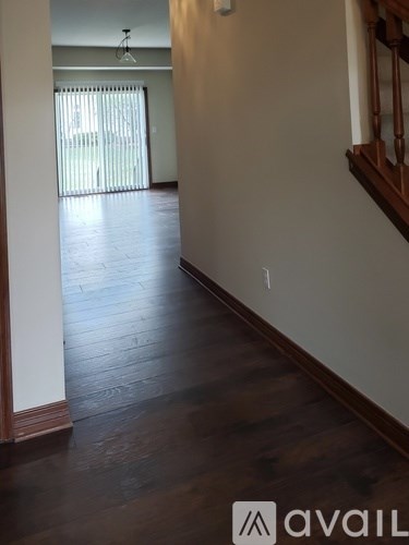A hallway with wood floors and a staircase on the right.