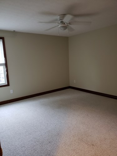 A room with a ceiling fan and carpeted floor.