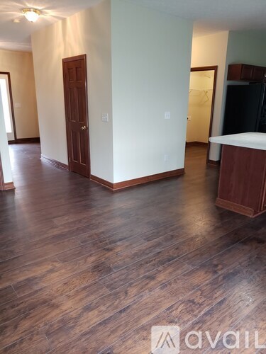 A room with wooden floors and a kitchen area with a refrigerator.