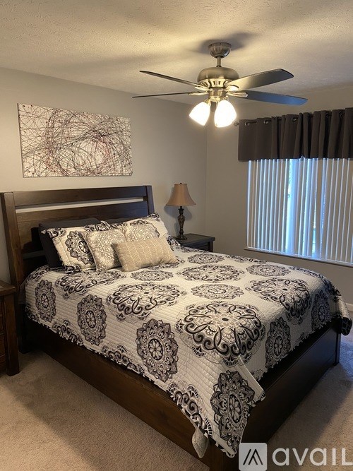 A bedroom with a bed, a ceiling fan, and a painting on the wall.