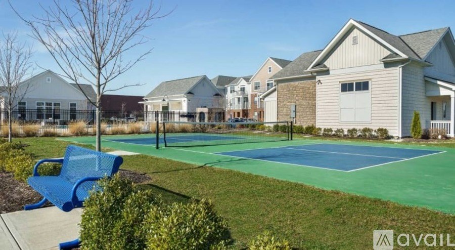 A tennis court is located in a grassy area in front of a row of houses.
