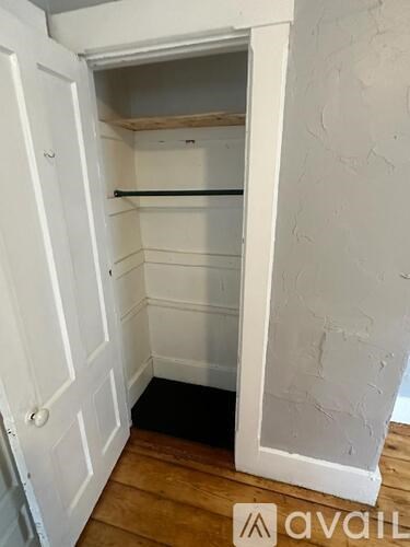 A white door is open to a small, empty room with wooden floors and white walls.