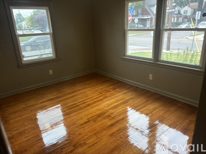 A room with wooden floors and two windows overlooking a street.