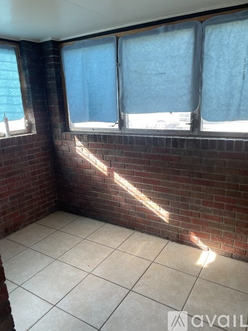 A room with brick walls and tiled floors has two windows covered with blue curtains.