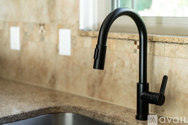 A black kitchen faucet with a pull-down sprayer is mounted on a beige countertop.