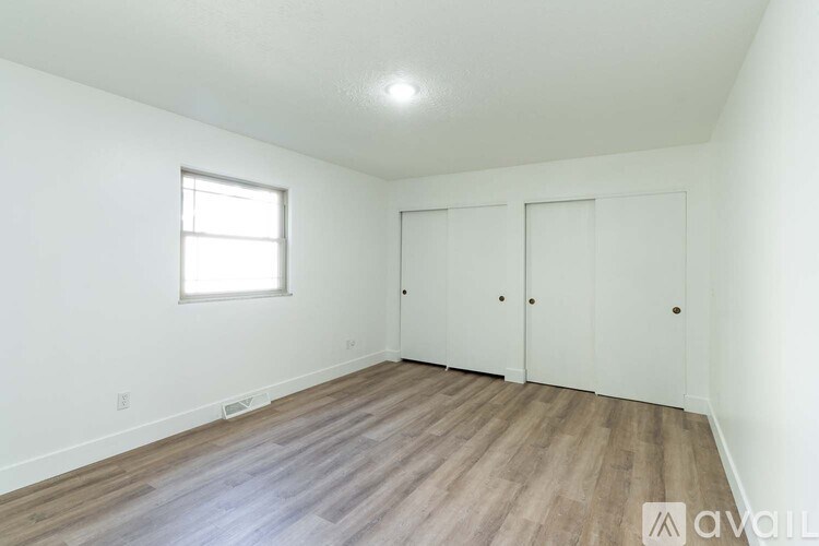 A room with wooden flooring and white walls, featuring a window and two doors.