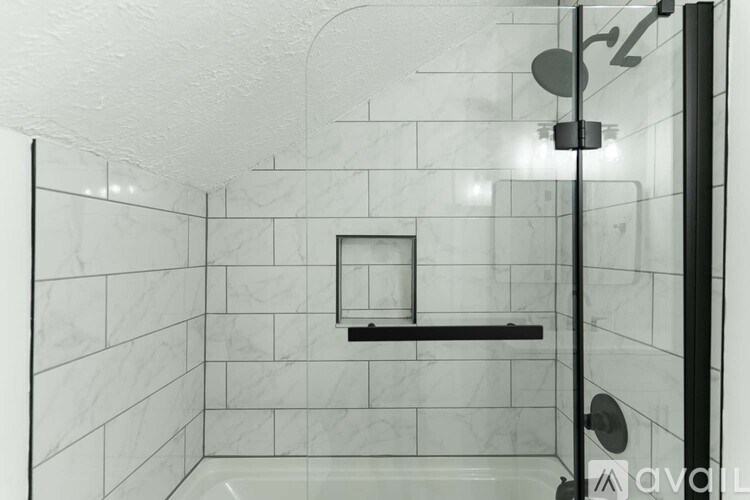 A white tiled shower with a black shower head and a black bar.
