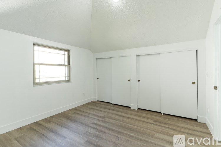 A room with a window, wooden floor, and white walls.