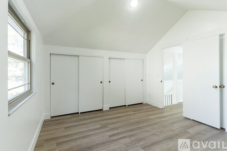 A room with white walls and wooden flooring, featuring a row of white closets and a door on the right.