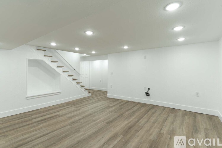 A spacious room with wooden flooring and a staircase.