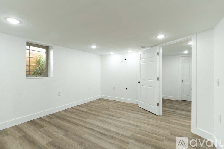 A room with wooden flooring and white walls, with a window on the left side.