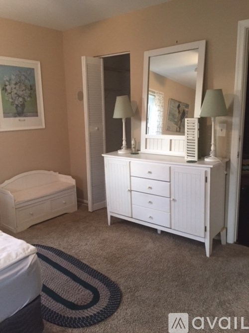 A bedroom with a white dresser and mirror, a white bench, and a painting on the wall.
