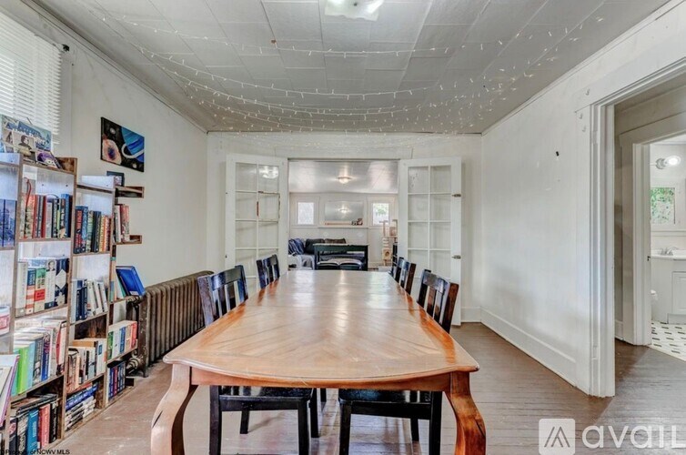 A room with a long wooden table surrounded by chairs and a bookshelf filled with books.