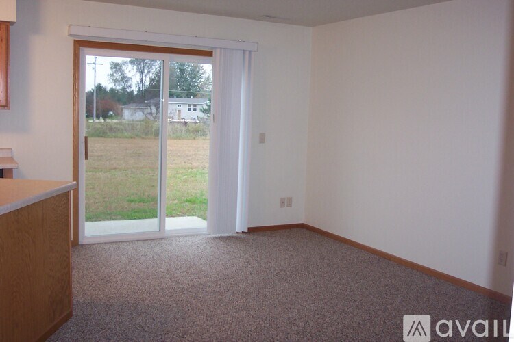 A room with a carpeted floor and a sliding glass door leading to a grassy area.