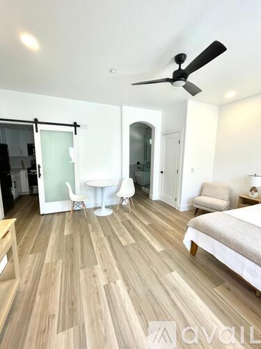 A bedroom with a bed, a table and chairs, and a ceiling fan.