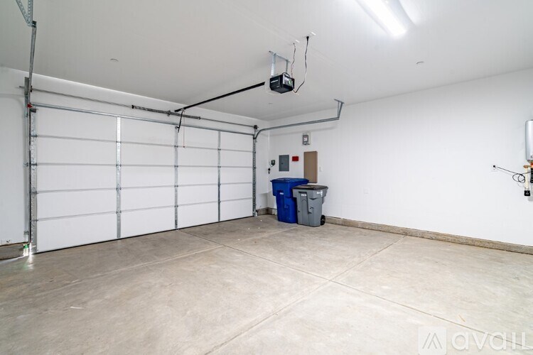 A large empty garage with a white door and a blue bin.