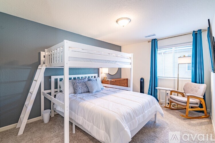 A white bunk bed with a white mattress and a white chair with a blue cushion.