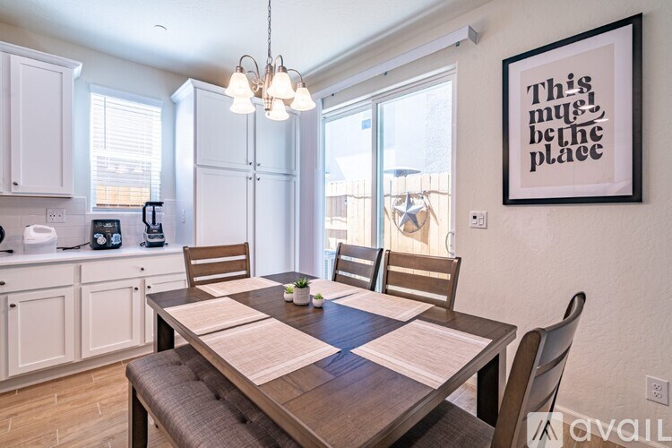 A dining room with a wooden table and chairs, a framed picture on the wall, and a window with blinds.