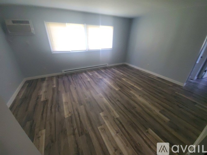 A room with wooden flooring and a window letting in sunlight.