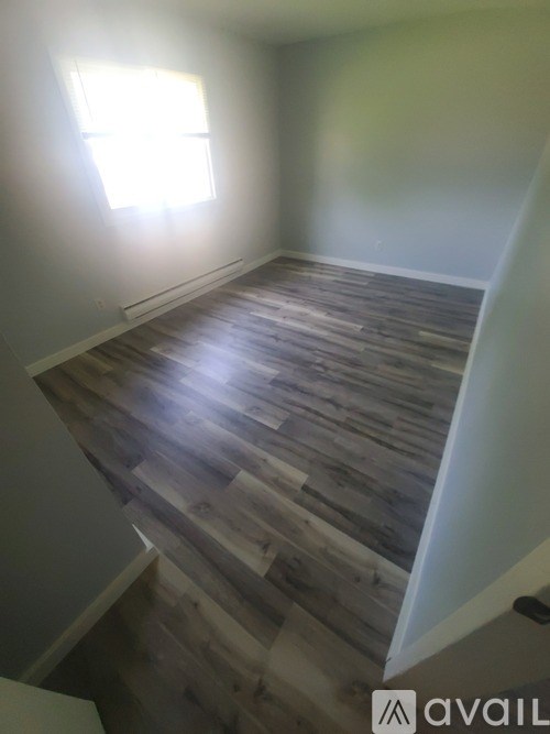 A room with wooden flooring and a window letting in sunlight.