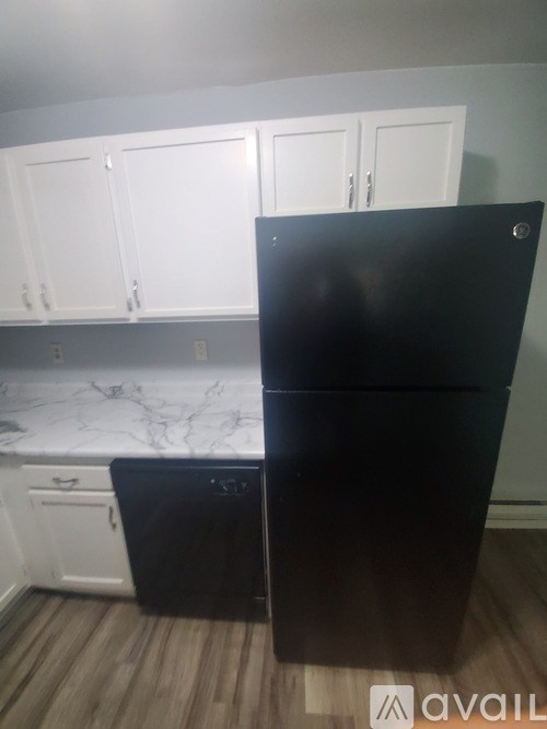 A black fridge in a kitchen with white cabinets.