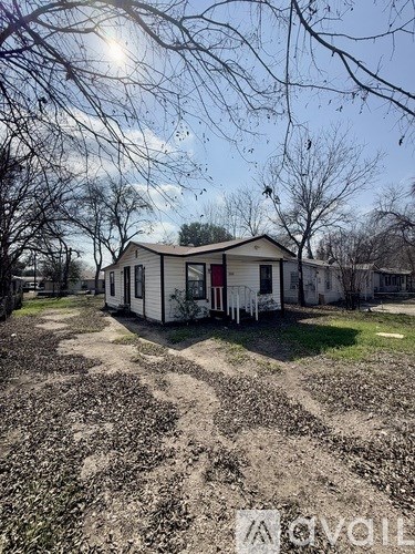 A small white house with a red door is surrounded by a field of cotton plants.