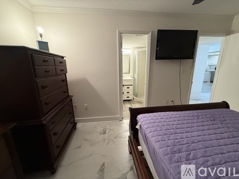 A bedroom with a purple bedspread and a wooden dresser.