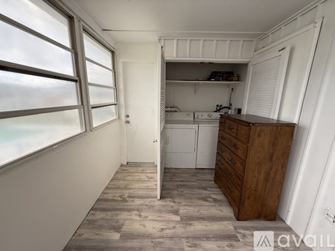 A kitchen area with a white fridge, wooden drawers, and a window with blinds.