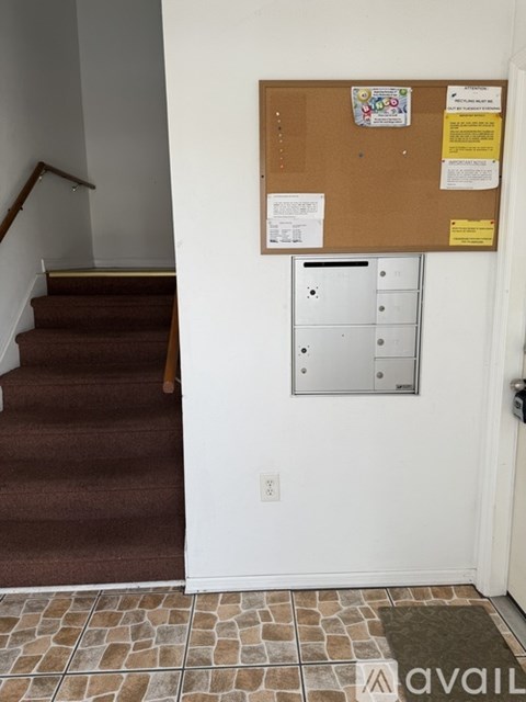 A bulletin board with several papers pinned to it is on a wall next to a staircase.