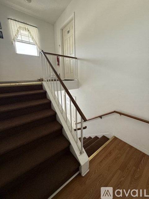A staircase with a wooden handrail and brown carpeted steps.