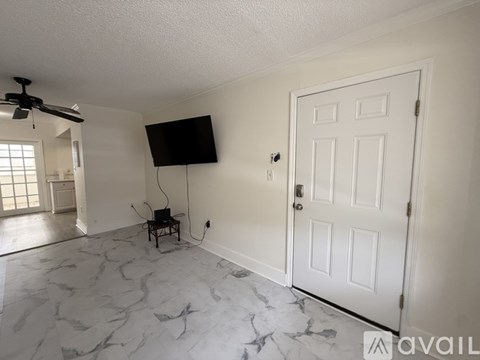 A room with a white door, a fan, and a flat screen TV mounted on the wall.