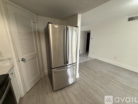 A stainless steel refrigerator stands in a kitchen with white cabinets and a wooden floor.