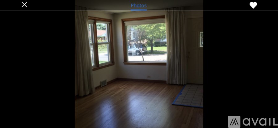 A room with wooden flooring and a large window with curtains.