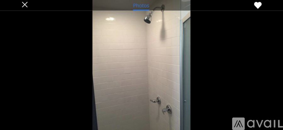 A white tiled bathroom wall with a shower head and a door.