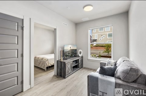 A modern living room with a grey couch and a large window showing an apartment building.
