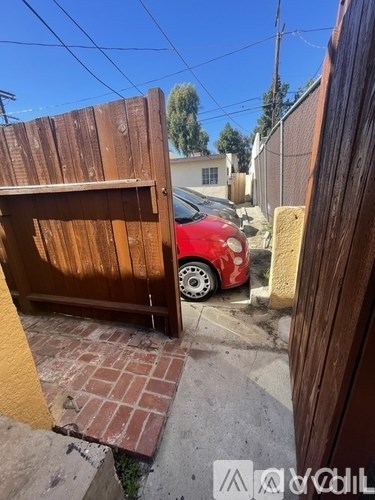 A red car is parked behind a wooden gate.