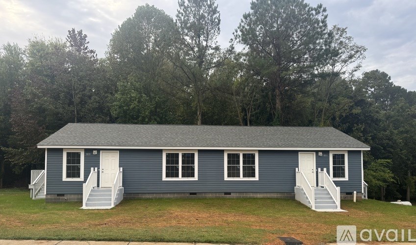 A blue house with white trim and a white door is surrounded by trees.