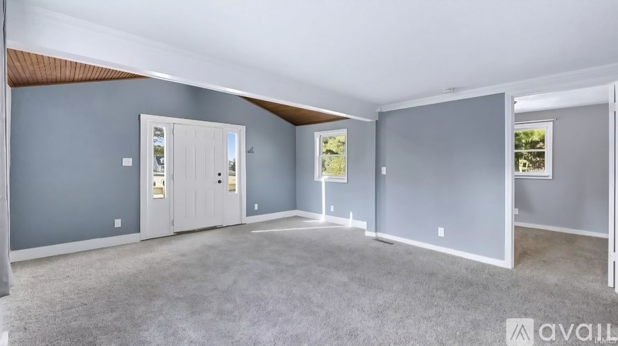 A spacious room with grey carpeting and white walls is available for rent.