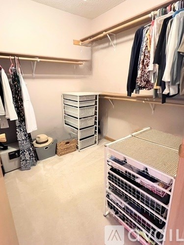 A small closet with clothes hanging on a rail and a pink drawer unit.