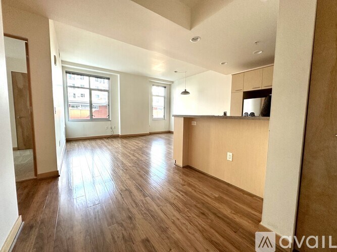 A spacious living room with wooden floors and a kitchen area in the background.