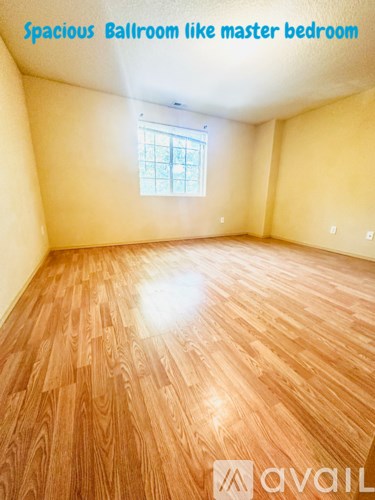 A spacious ballroom like master bedroom with wooden flooring and a window.