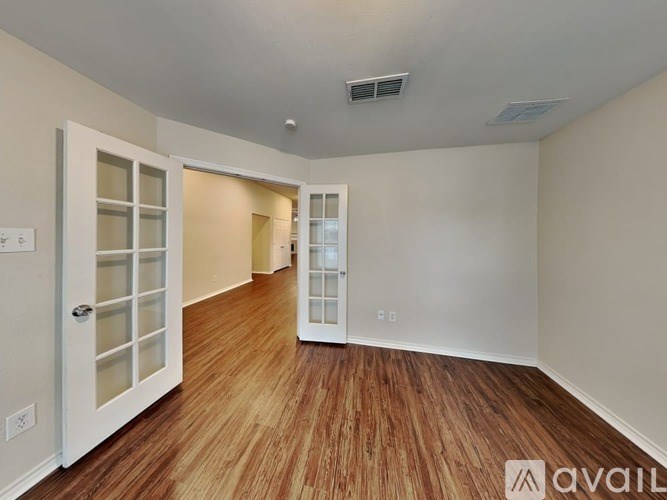 A room with wooden flooring and white walls, with a door on the left and a window on the right.